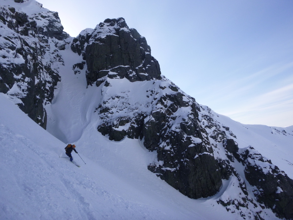 Lone skier descending past jagged rock face on Lyngen Alps ski tour, Norway