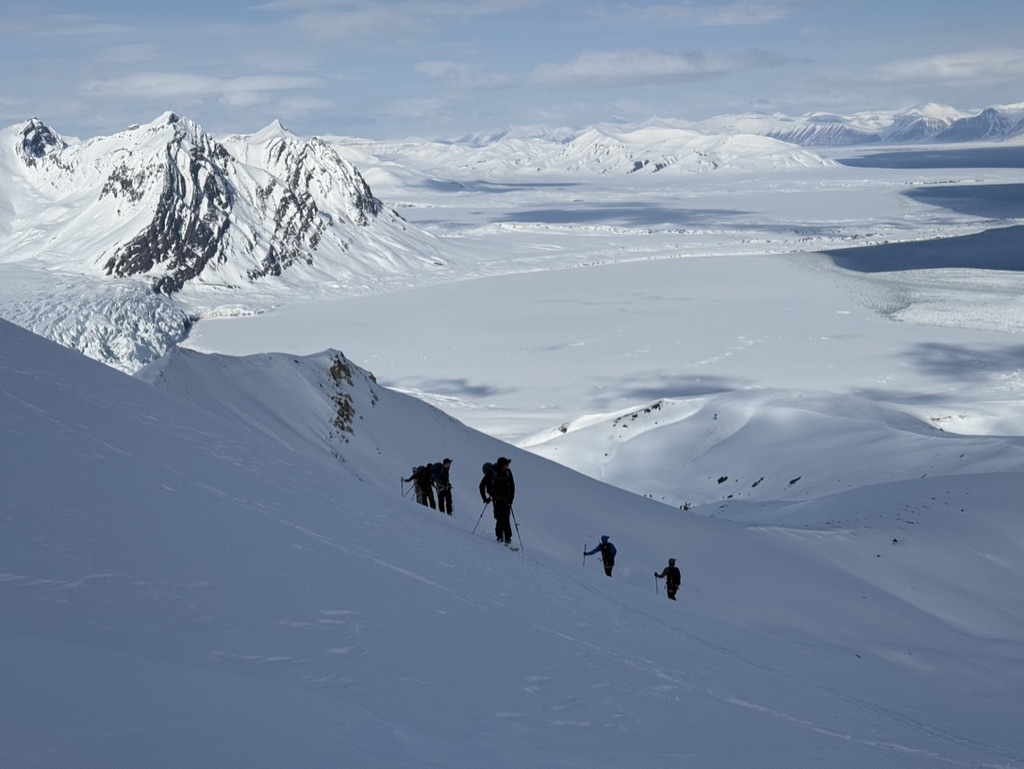 Group skinning up Svalbard ridge with frozen sea ice bay in background
