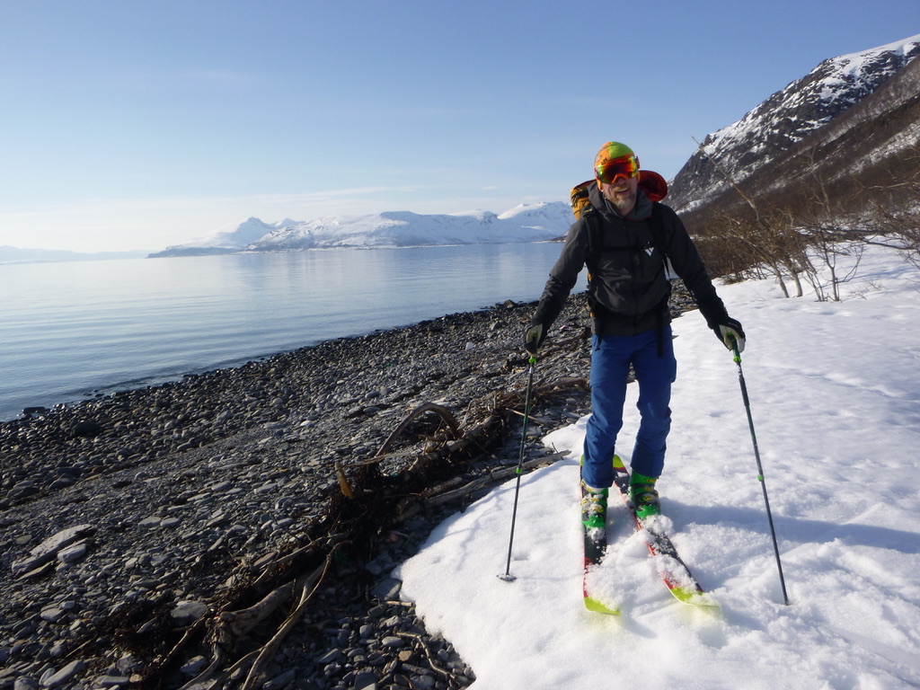 Skier standing on snow-covered shore beside Lyngen Alps fjord, Norway