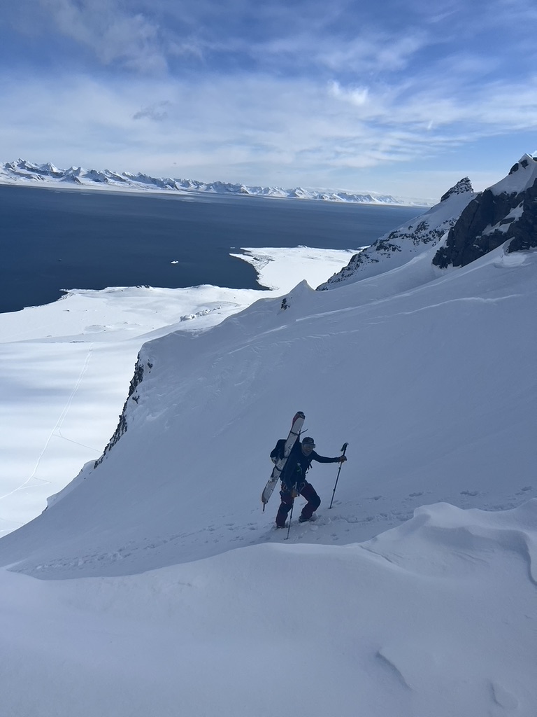 IFMGA guide bootpacking with skis on Svalbard summit ridge above ice-filled fjord