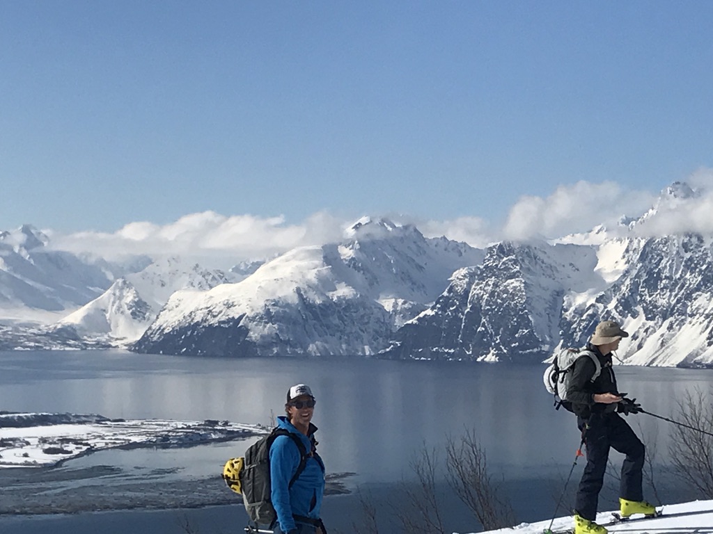 Two skiers pausing on snowy ridge overlooking fjord and snow-capped peaks in the Lyngen Alps, Norway