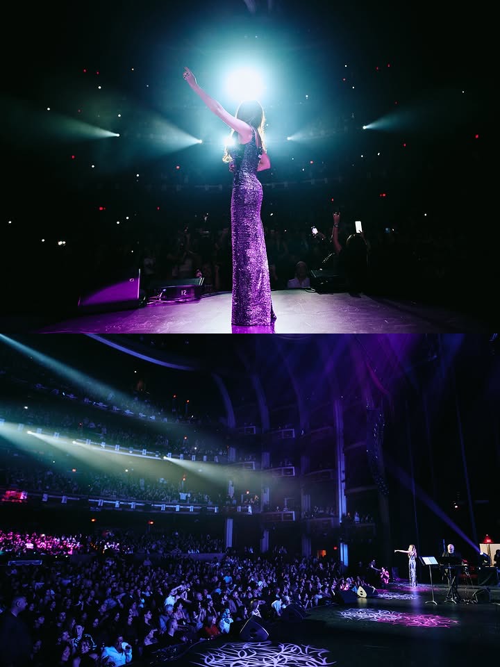 A live concert performance with a performer center stage under a bright spotlight, dramatic stage lighting, and a packed theater audience silhouetted in the dark. Live Pros concert and live music production.
