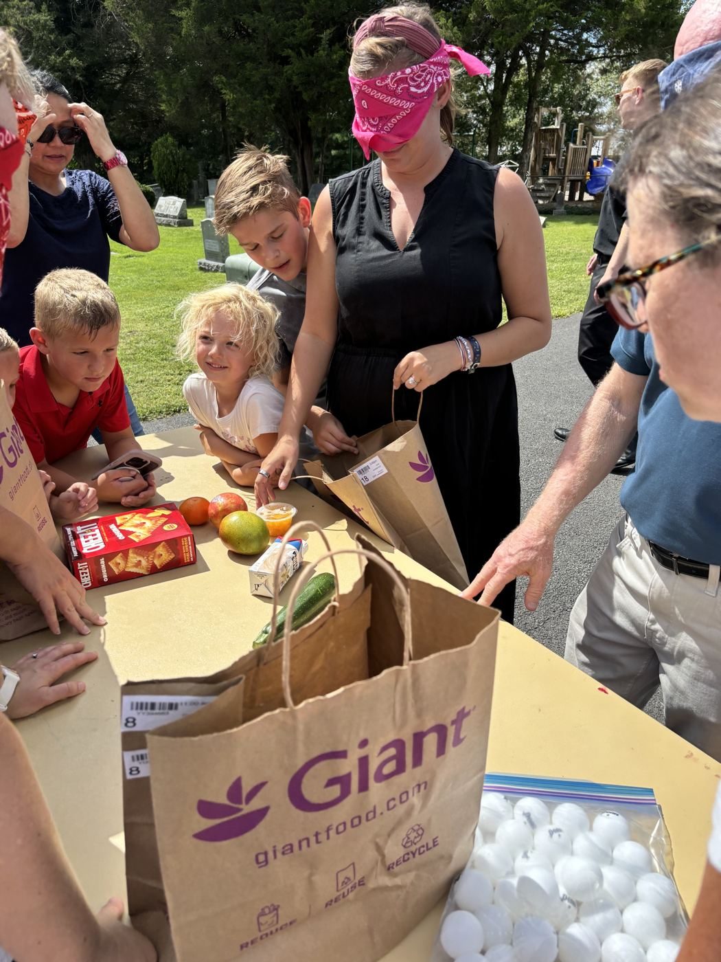 A blindfolded woman reaches into a paper grocery bag during a guessing game