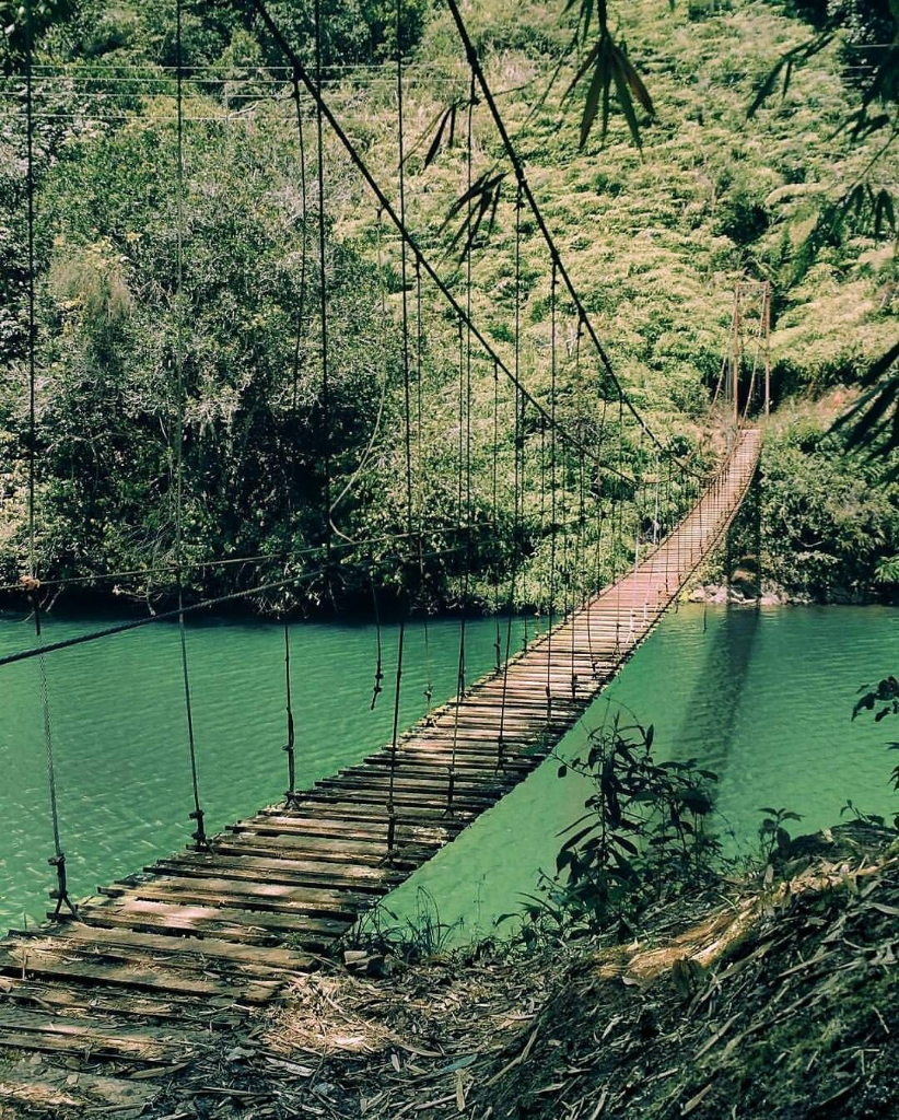 Suspension bridge over a turquoise river surrounded by lush green jungle