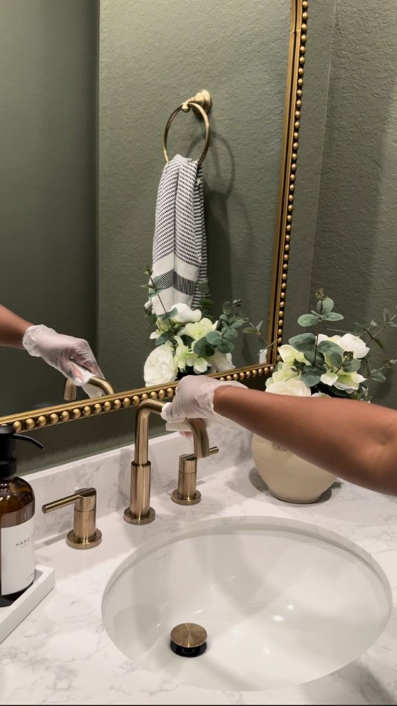 Professional cleaner wiping down a brushed-gold bathroom faucet