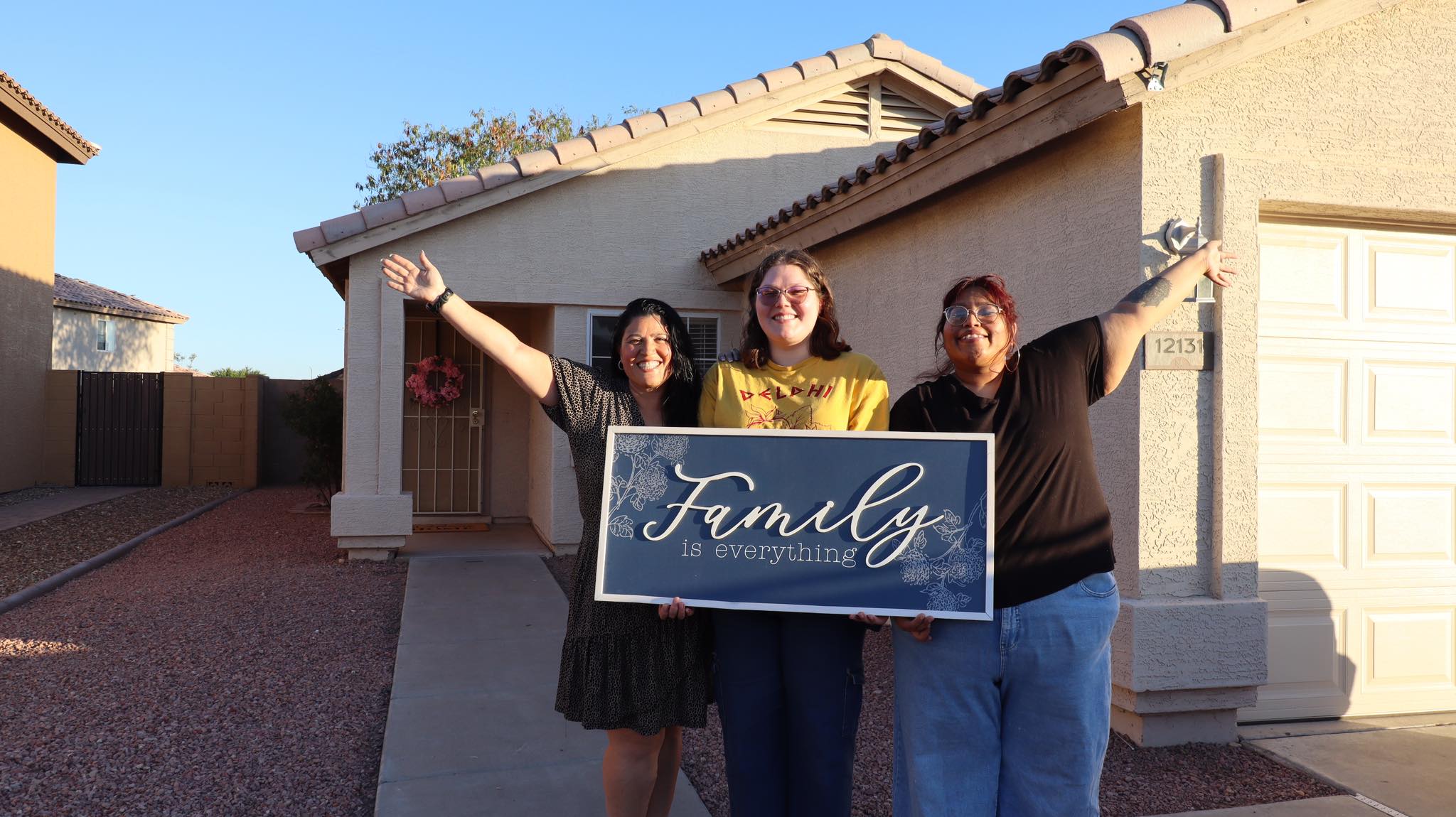 Three women holding a Family is Everything sign in front of their home