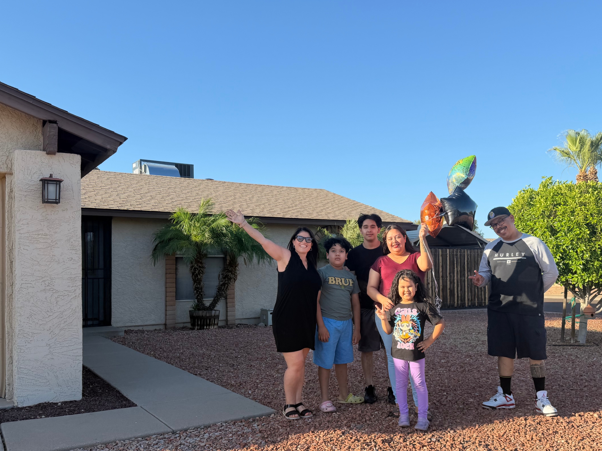 Family of six waving in front of their new stucco home