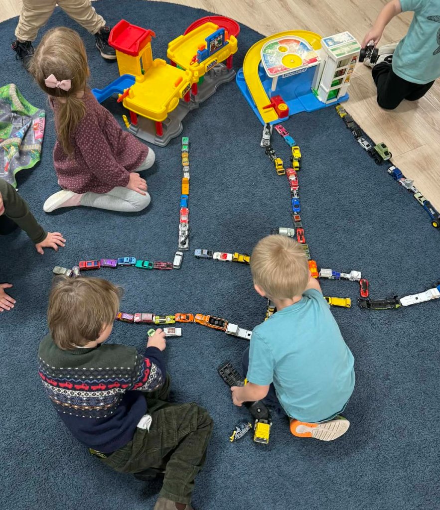 Children lining up toy cars on the classroom rug