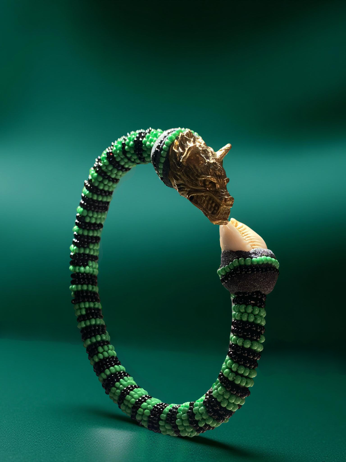 Green and black beaded ildé with a carved metallic ram's head and a cowrie shell