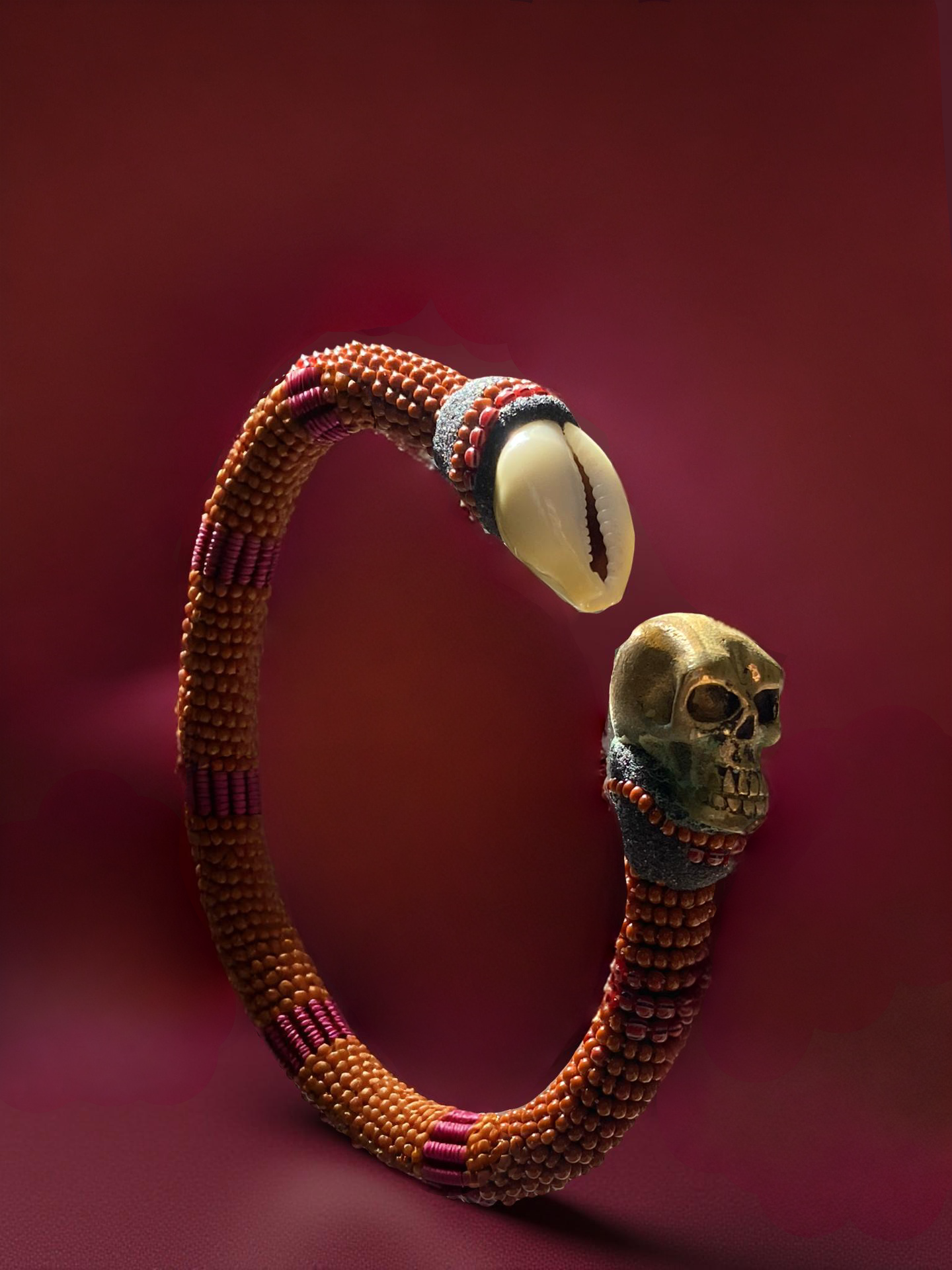 Orange and maroon beaded ildé finished with a brass skull and a cowrie shell