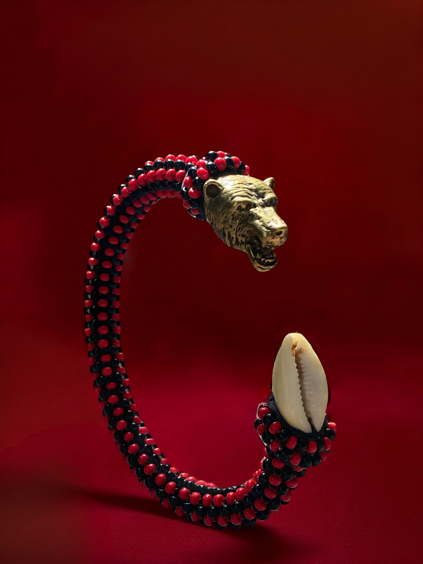 Red and black beaded ildé with a carved metallic feline head and a cowrie shell