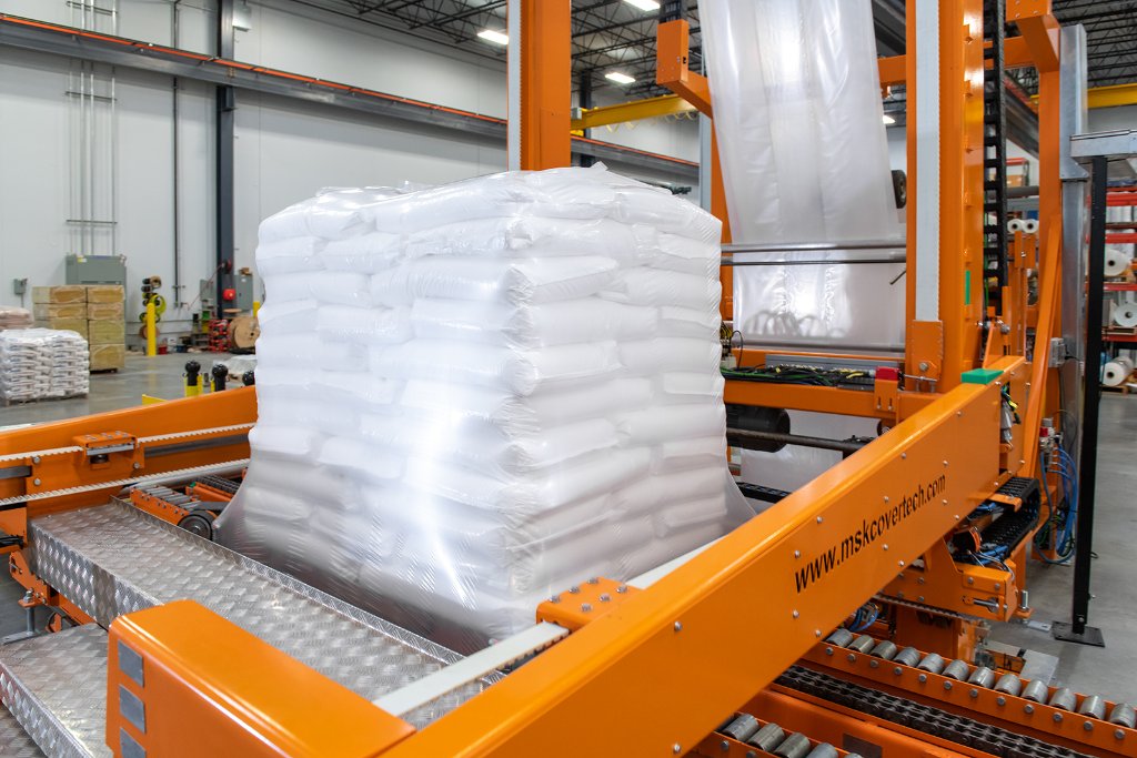 Stretch hood film being stretched and applied over a pallet load by an automated stretch hood machine
