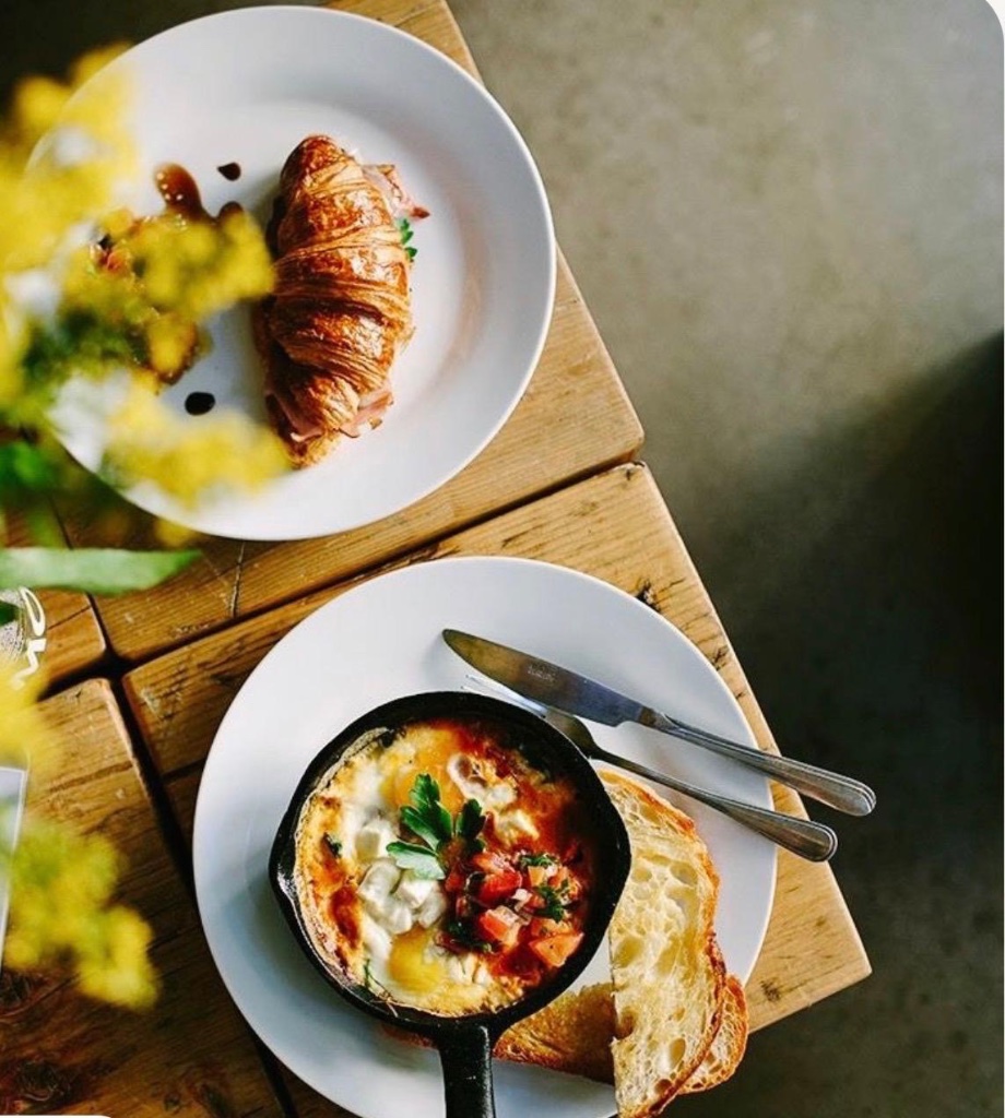 Artisanal breakfast dishes including croissant and shakshuka on a wooden table