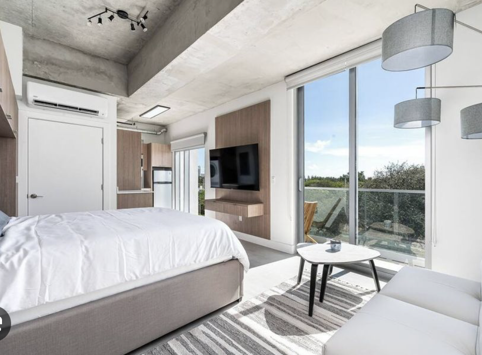 Modern studio suite with exposed concrete ceiling, king bed, wood accents and city view balcony