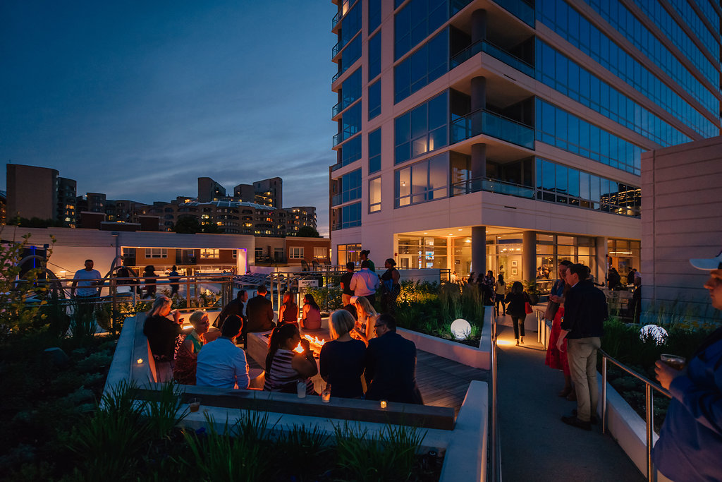 Residents gathered around a fire pit on a rooftop terrace at dusk