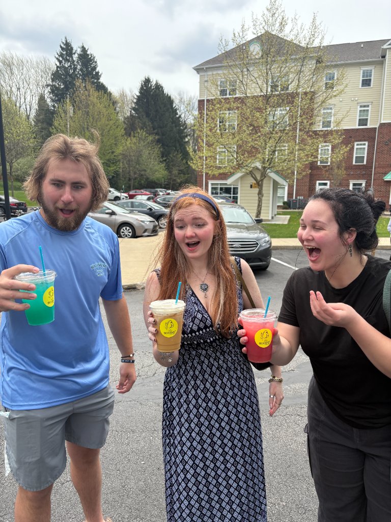 Three people holding Boobys drinks in a parking lot