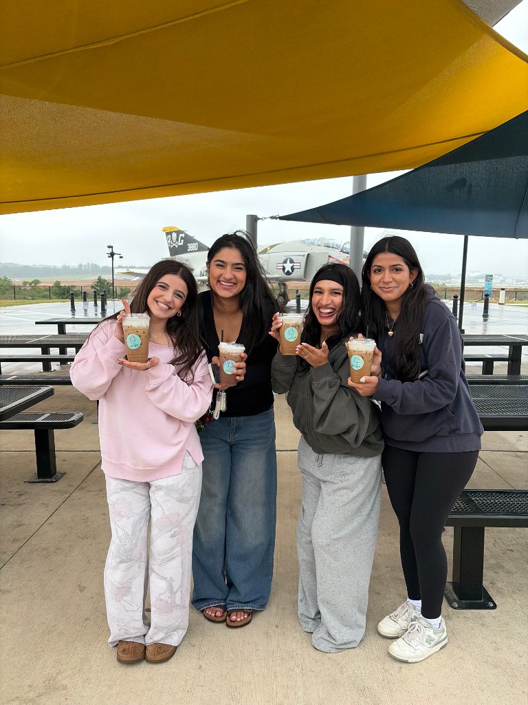 Four women holding iced coffee drinks in front of an aircraft