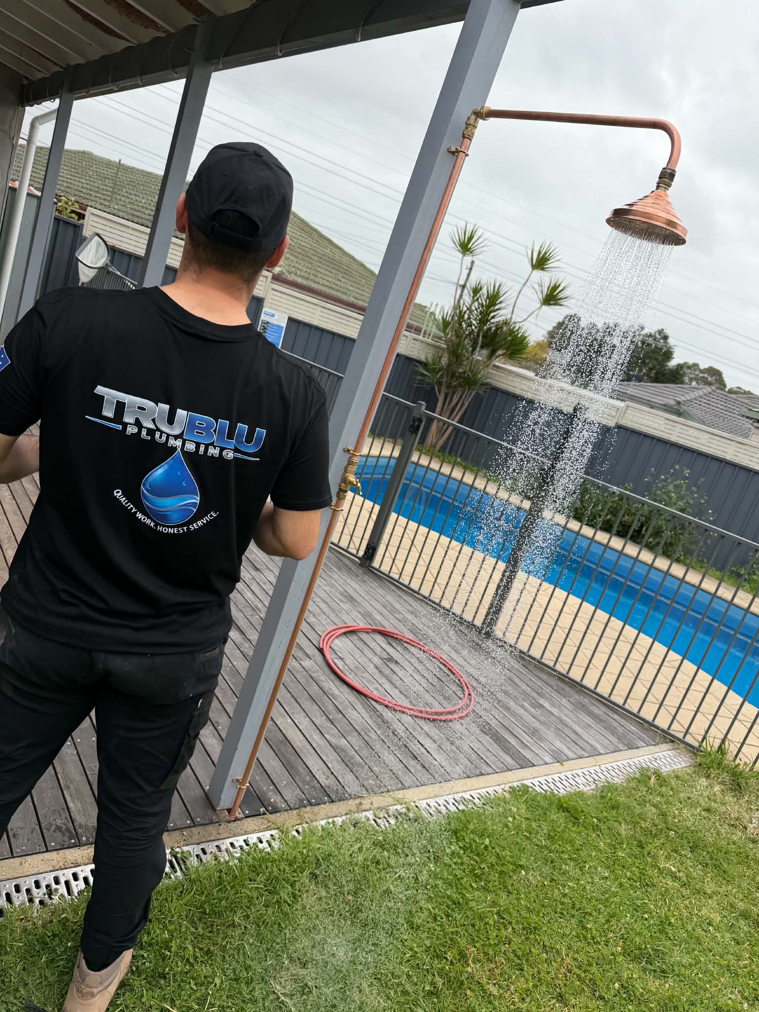 Tru Blu plumber installing an exposed copper outdoor shower with water running on a backyard deck