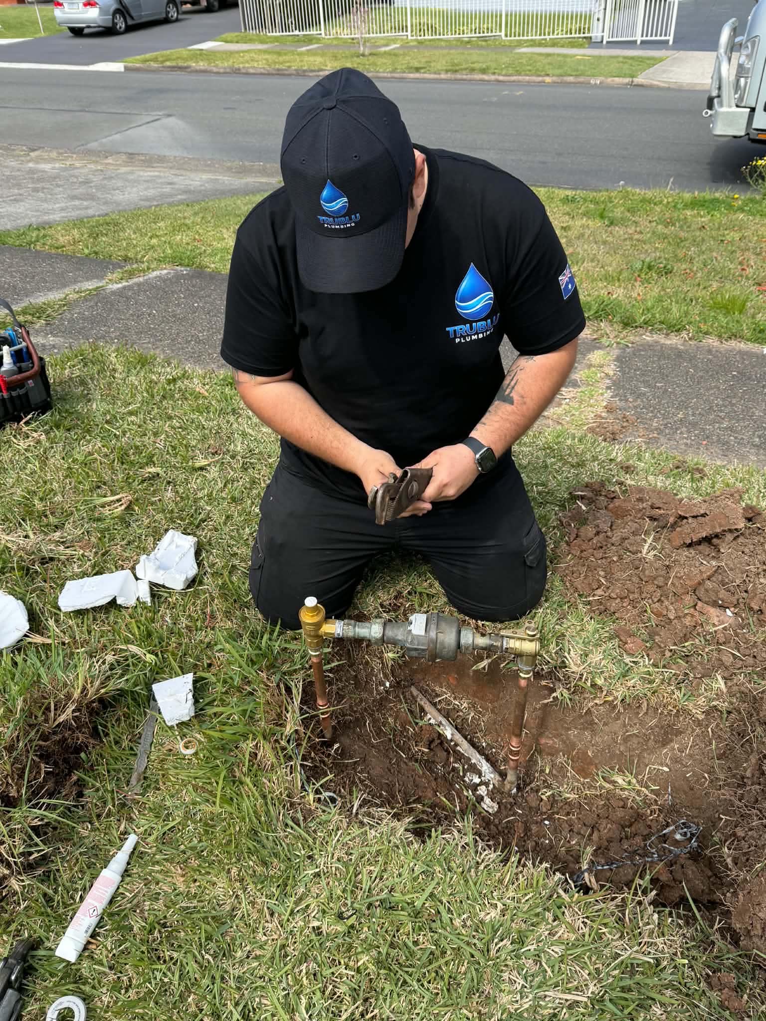 Tru Blu plumber kneeling on a lawn connecting a brass water meter assembly to copper pipes