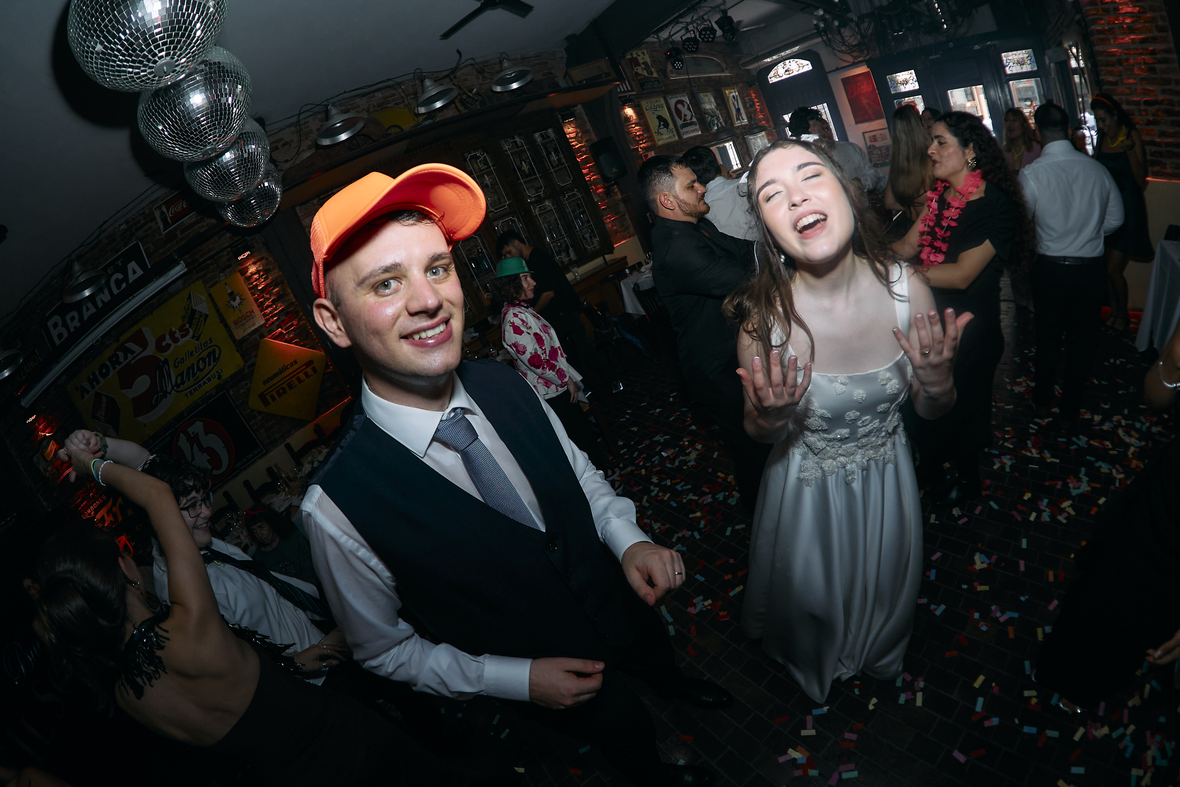 La novia y los invitados cantando en la pista con gorros de cotillón y papel picado
