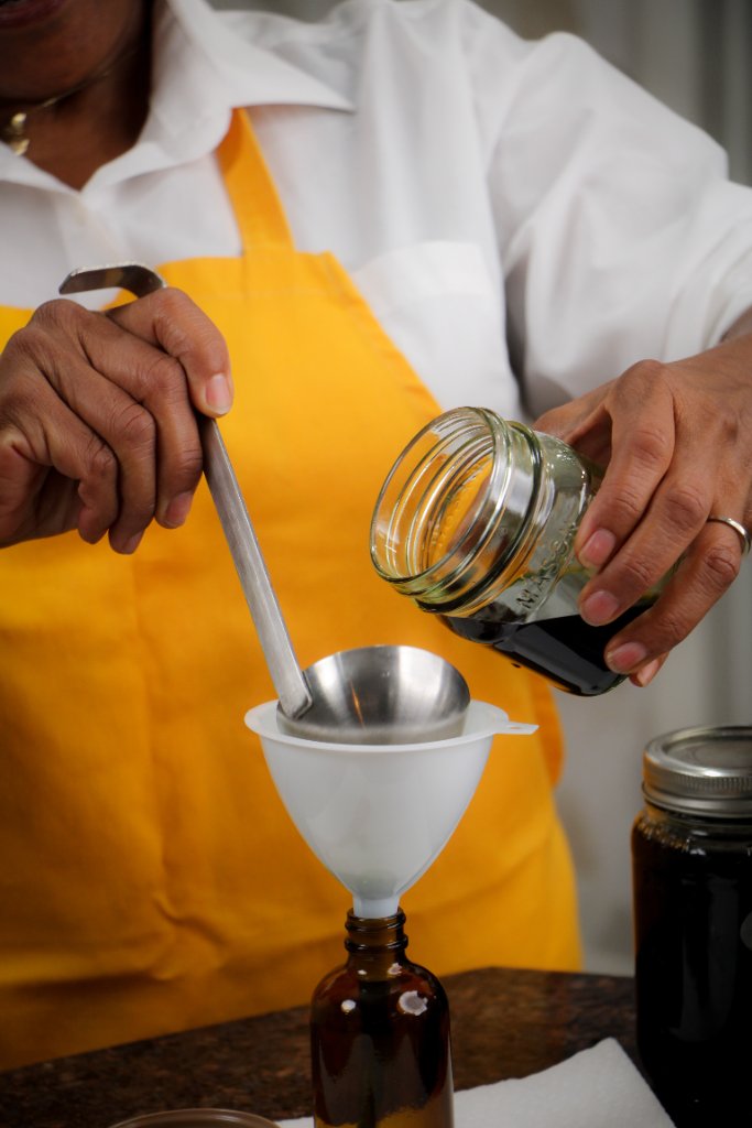Dr. Debbie carefully pouring a herbal tincture into amber bottles