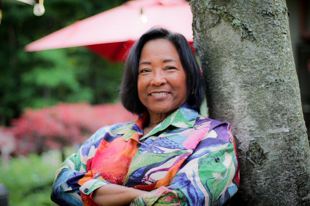Dr. Debbie smiling warmly while leaning against a tree in a lush garden