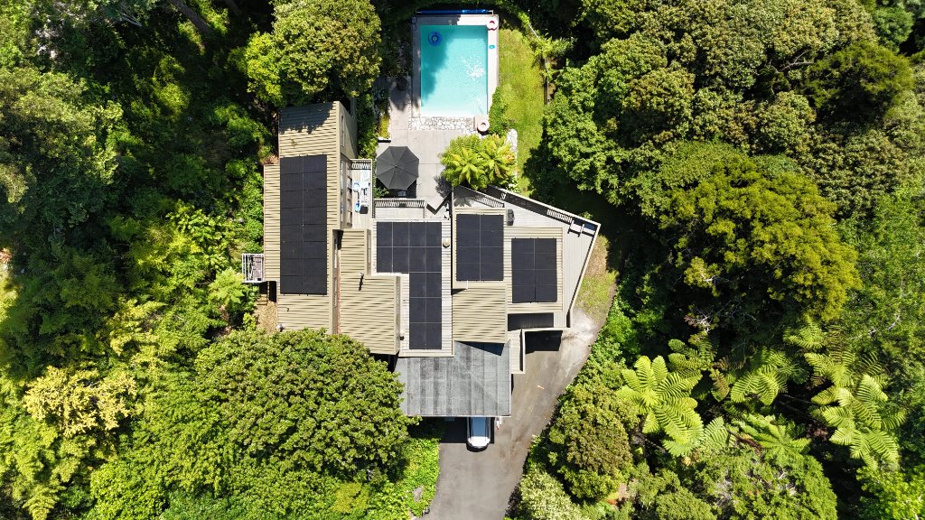 Aerial view of a residential solar installation on a house surrounded by mature trees in a Waikato gully