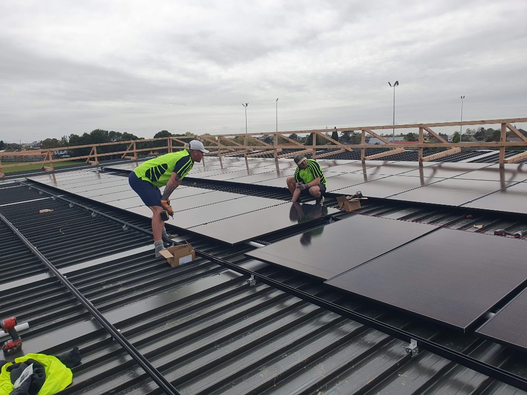 2E Electrical installers fitting solar panels on the Pukete Neighbourhood House roof