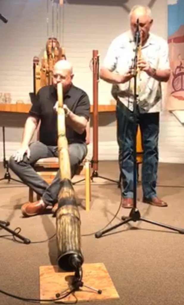 Ron playing a didgeridoo indoors alongside a flutist