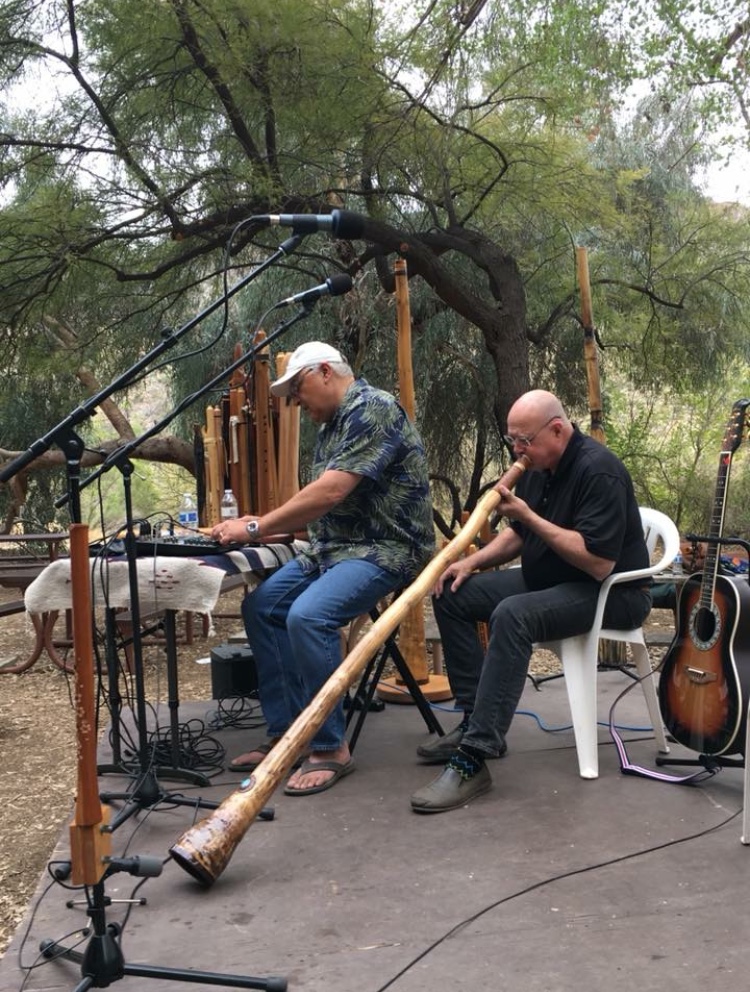 Ron playing a didgeridoo on an outdoor stage with a fellow musician