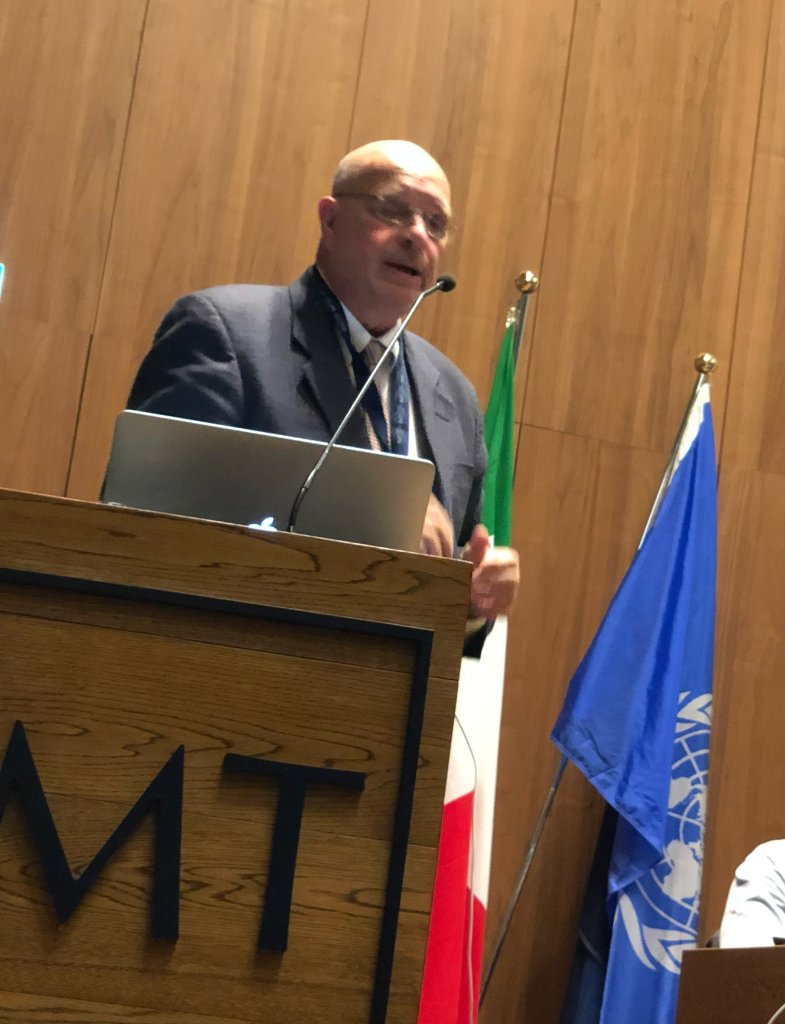 Ron Bonnstetter speaking at a podium during an international conference
