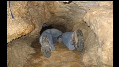Caver crawling through a narrow cave passage