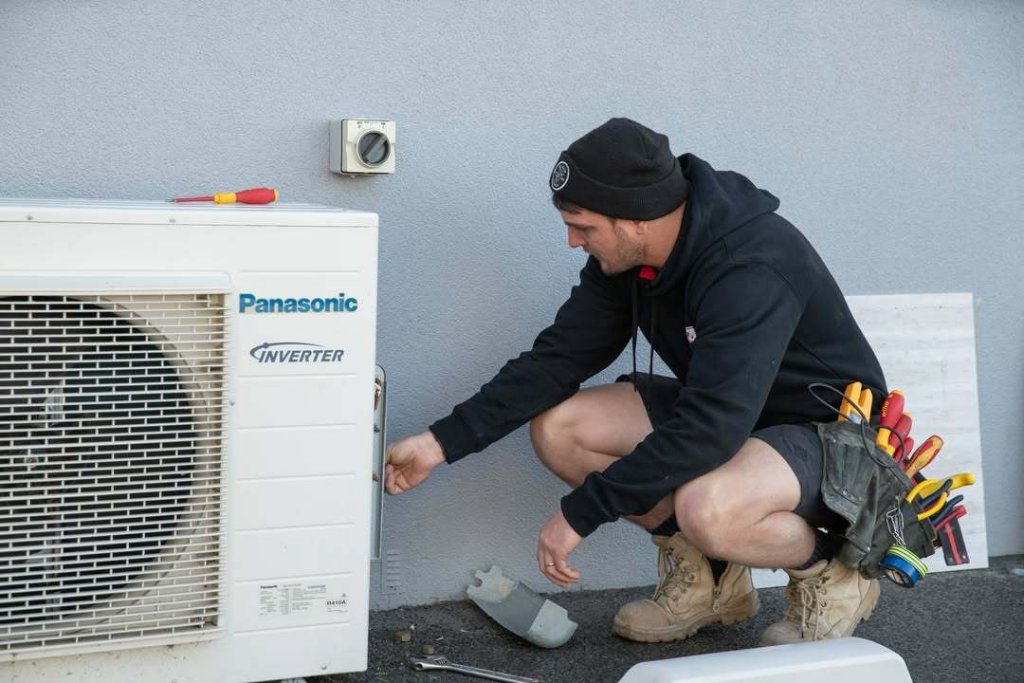 Electrician professionally installing a heat pump unit on a wall