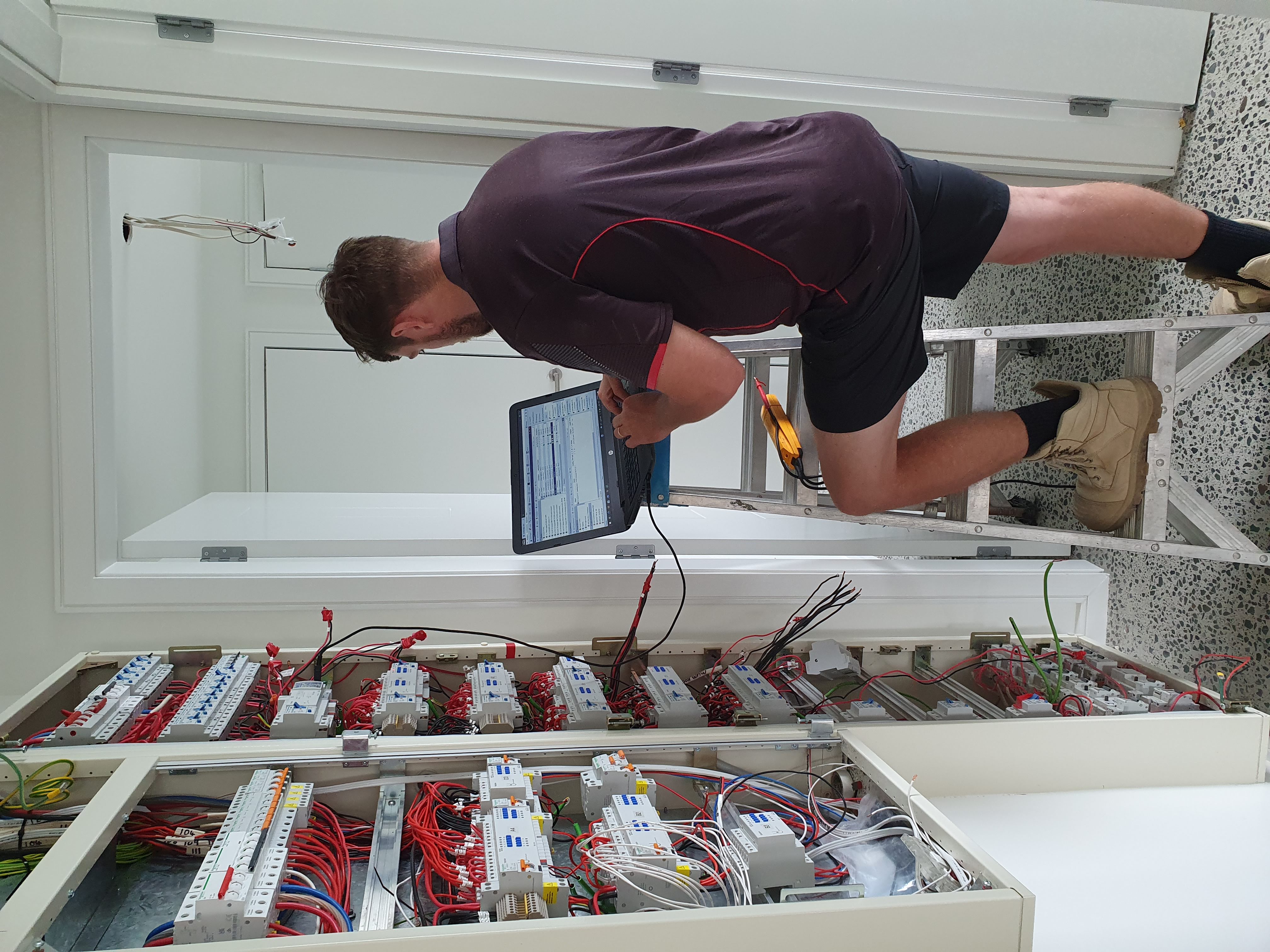 A 2E Electrical electrician using a laptop to test and monitor an electrical switchboard on site