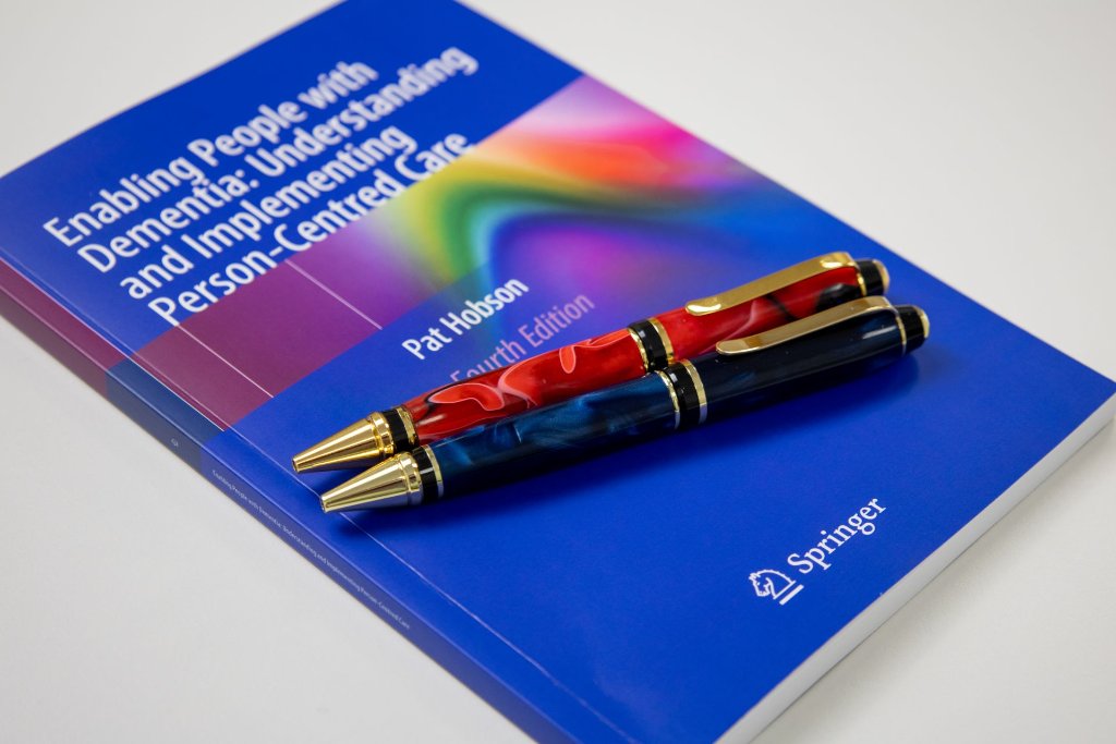Pat Hobson's dementia care book photographed at an angle alongside pens on a professional desk