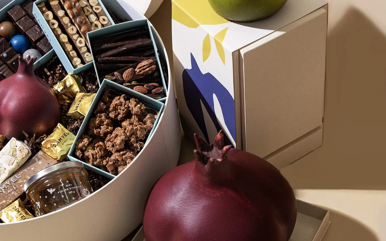 Coffret de chocolats DAMYEL ouvert, avec une grenade et une pomme