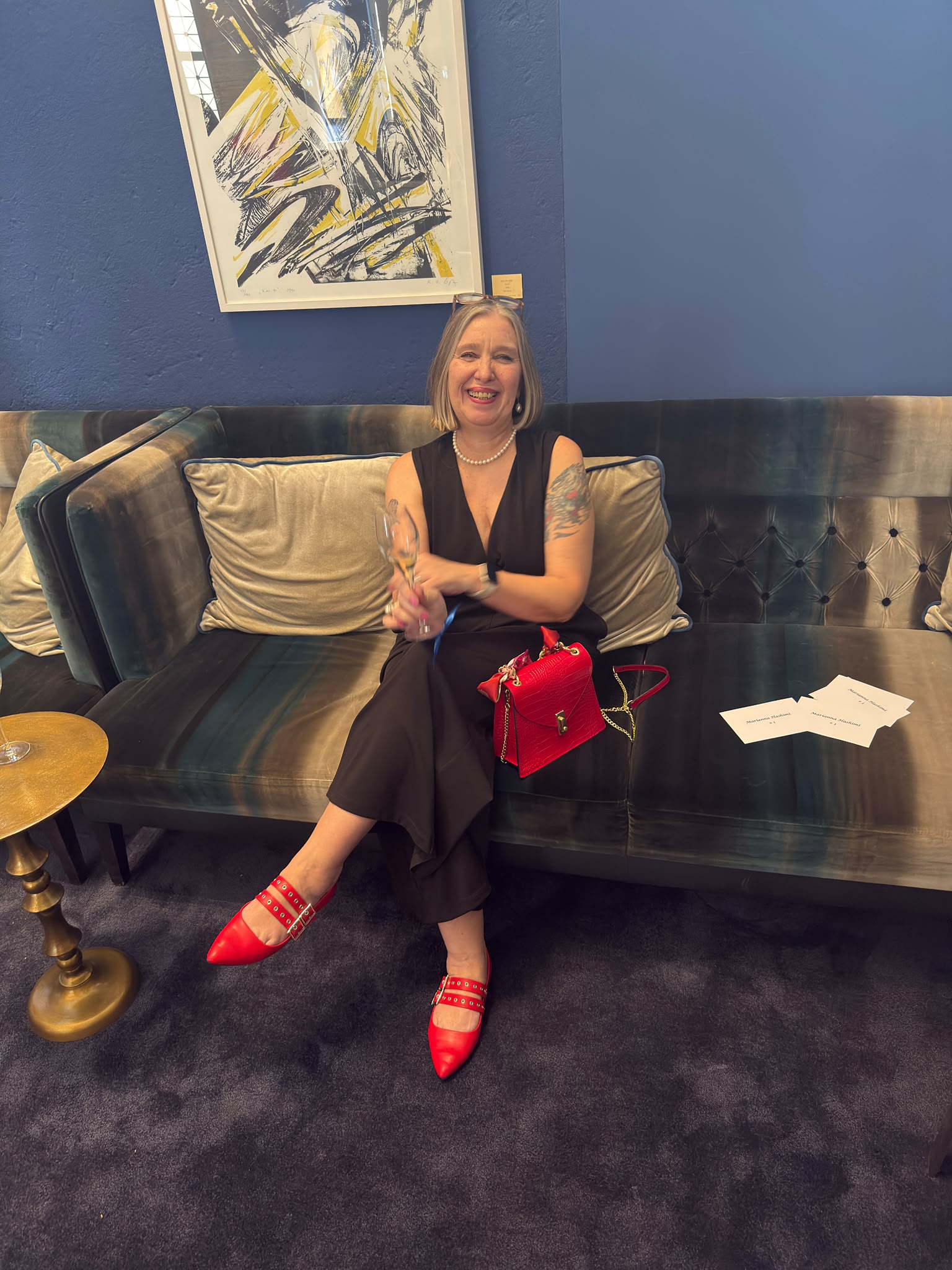 Christiane elegant auf einer Samtbank sitzend mit roter Handtasche – Beauty und Stil für Best Ager