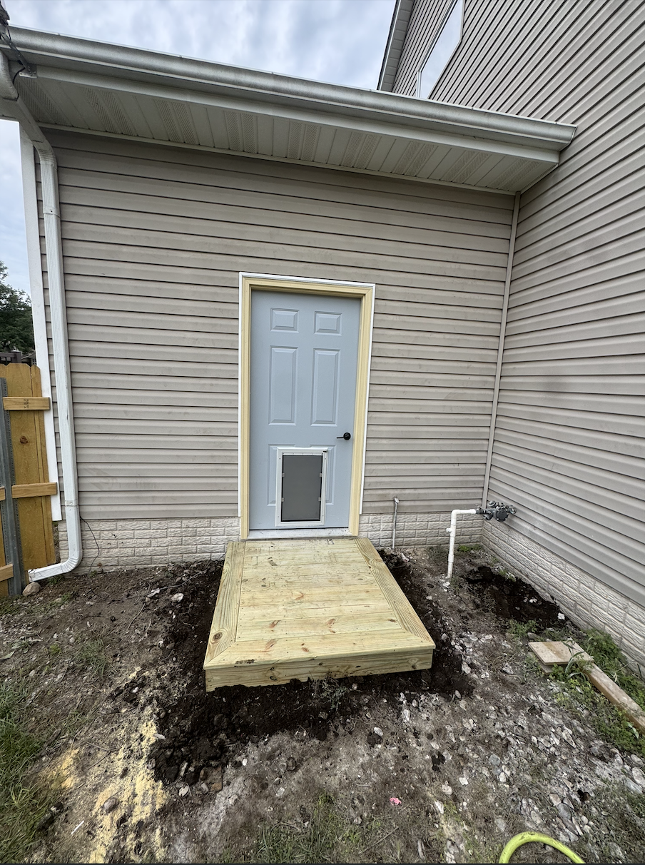 New six-panel steel utility door with pet door and custom picture-frame step installed in a garage wall