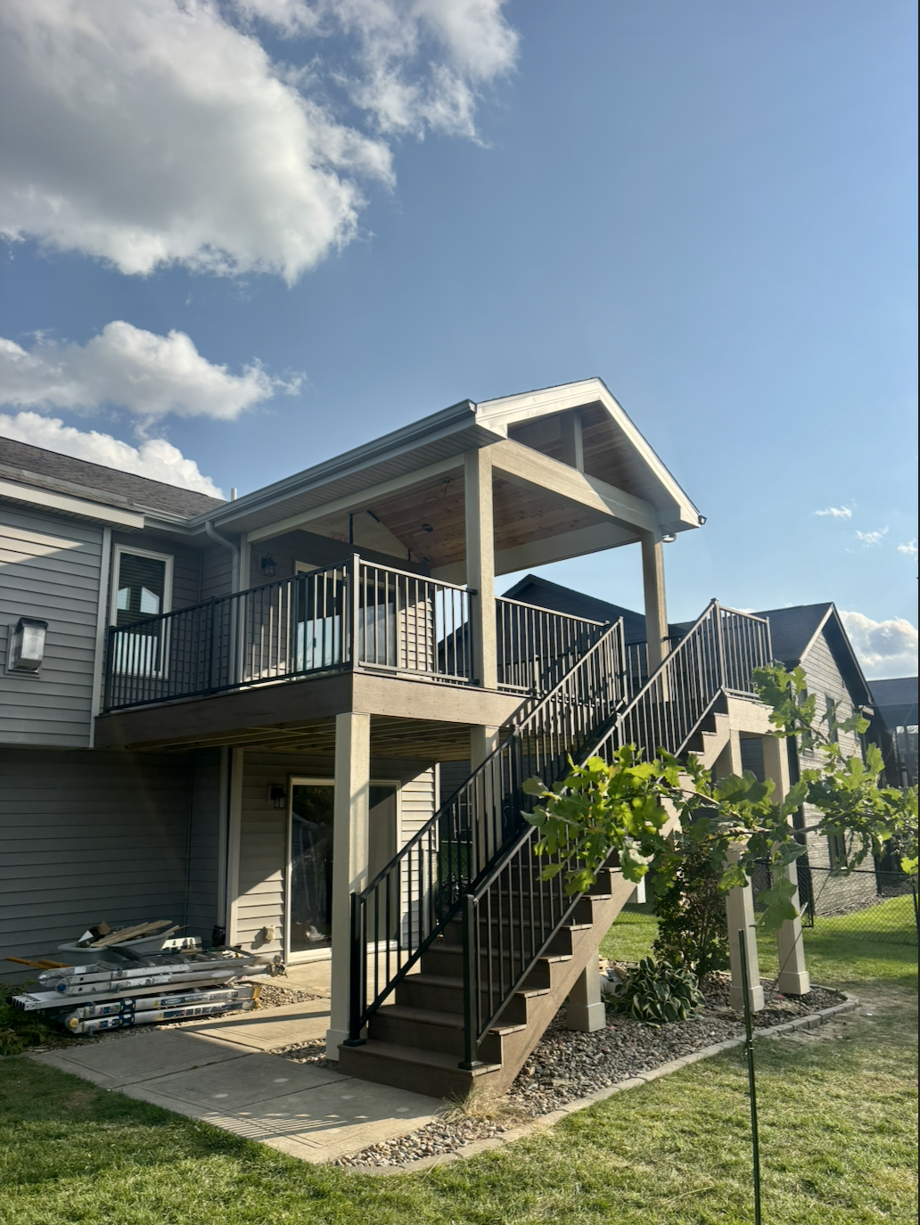 Covered composite deck with wood ceiling, black railing, and wide staircase built by Akin Brothers Construction in Ankeny