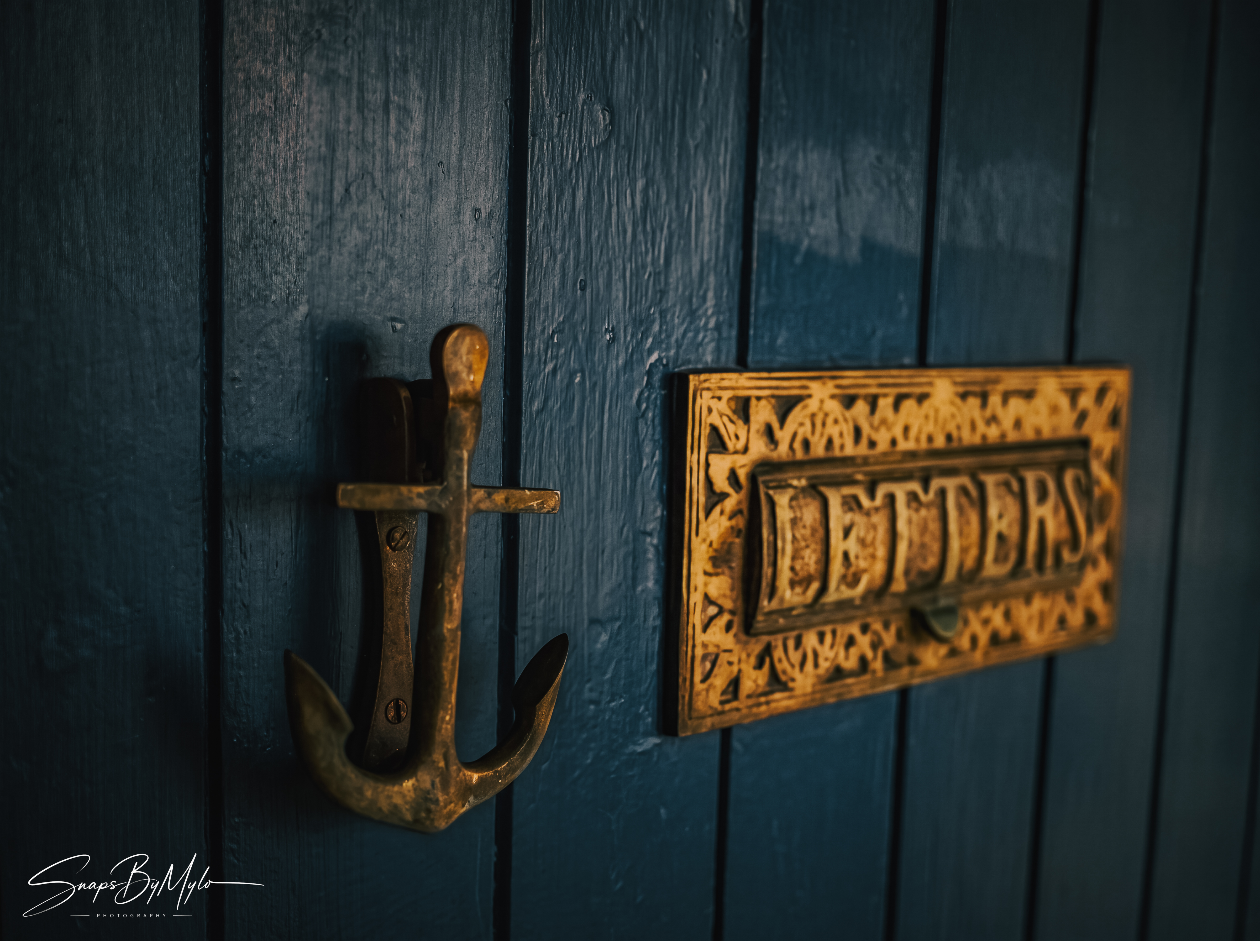 A brass anchor door knocker and ornate letter slot on a dark navy wooden door