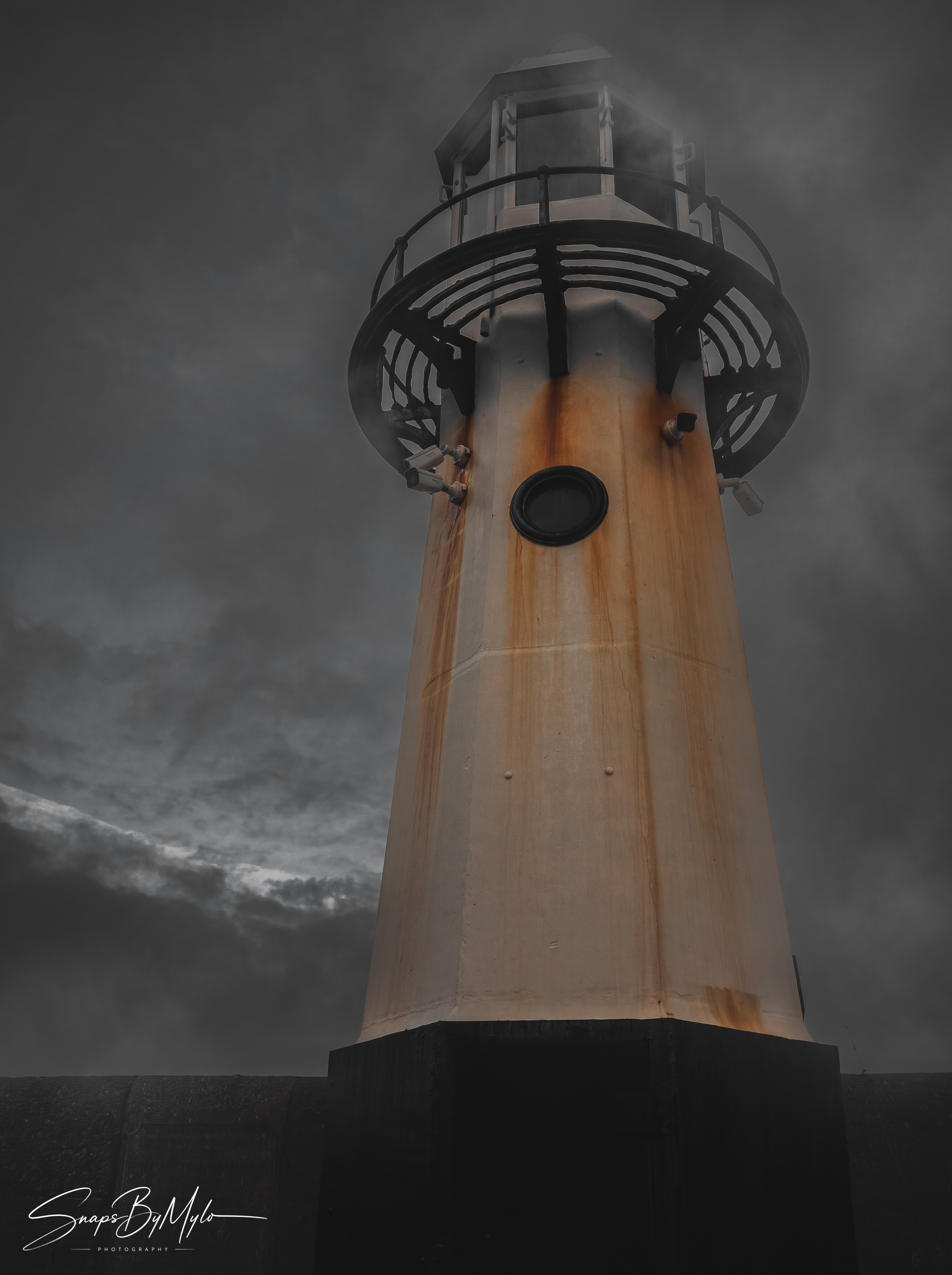 A weathered white lighthouse tower against a dark, moody overcast sky