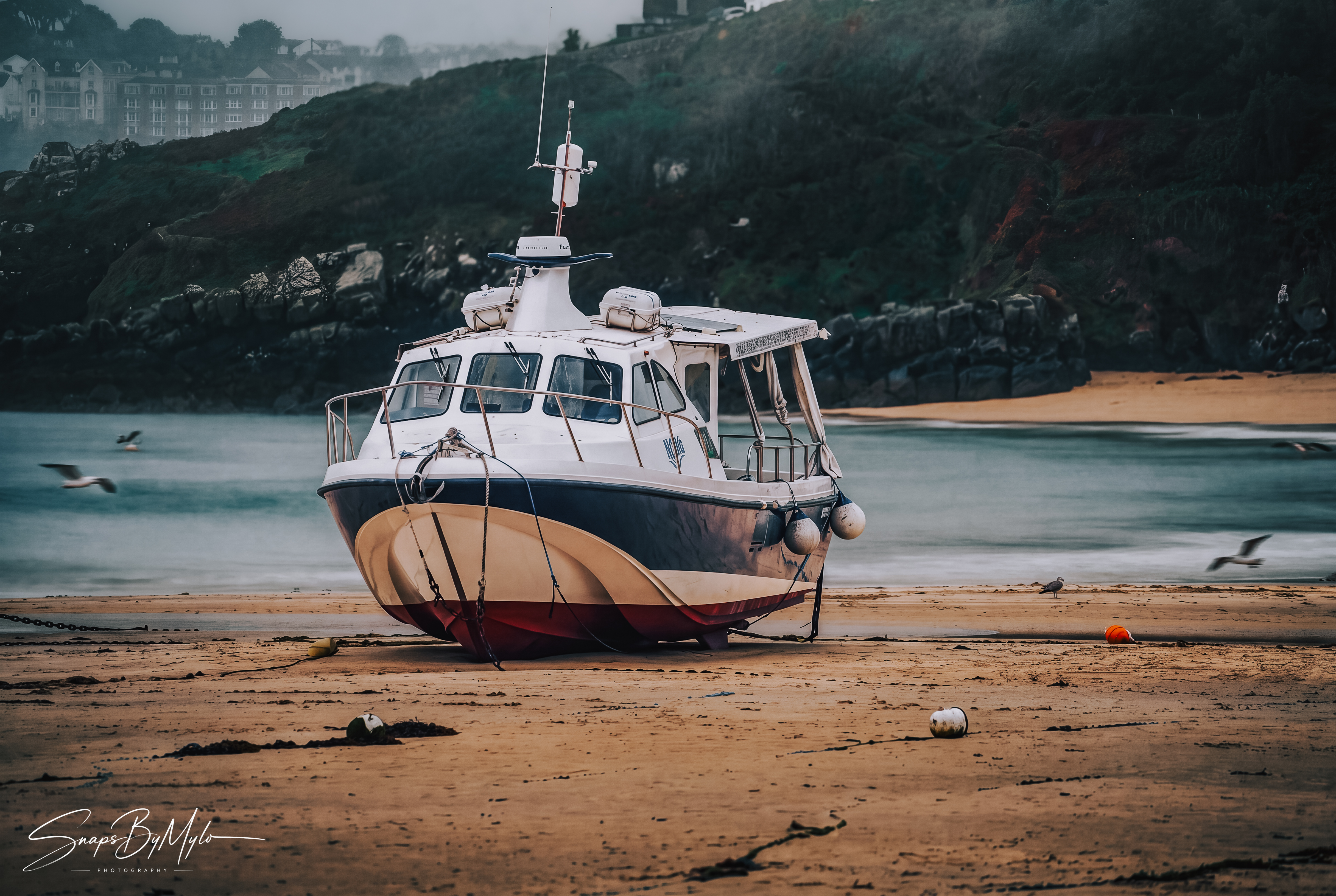 A white motorboat with blue and red hull resting on the wet sand of a St Ives beach