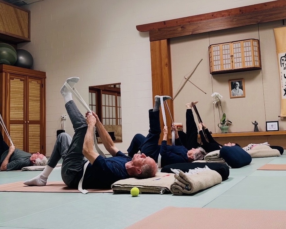 Seniors in a therapeutic yoga class lying on mats using straps