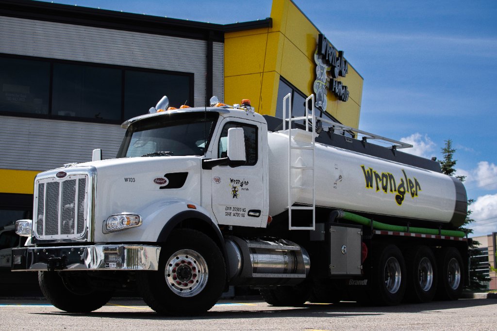 White Peterbilt water truck with Wrangler Rentals branding in front of a yellow building