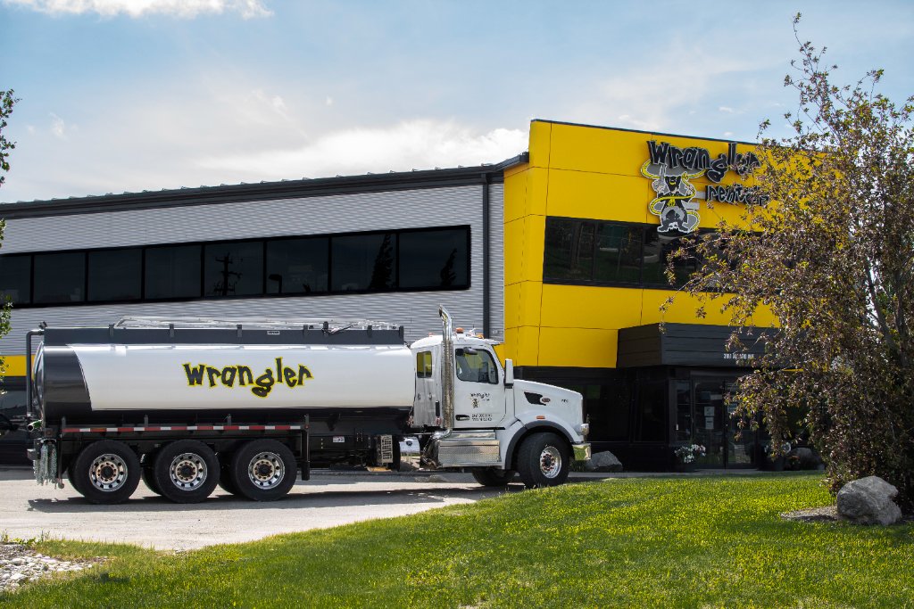 White Wrangler Rentals water tanker truck parked in front of yellow industrial building