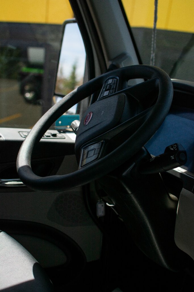 Interior close-up of truck steering wheel with yellow building visible through window