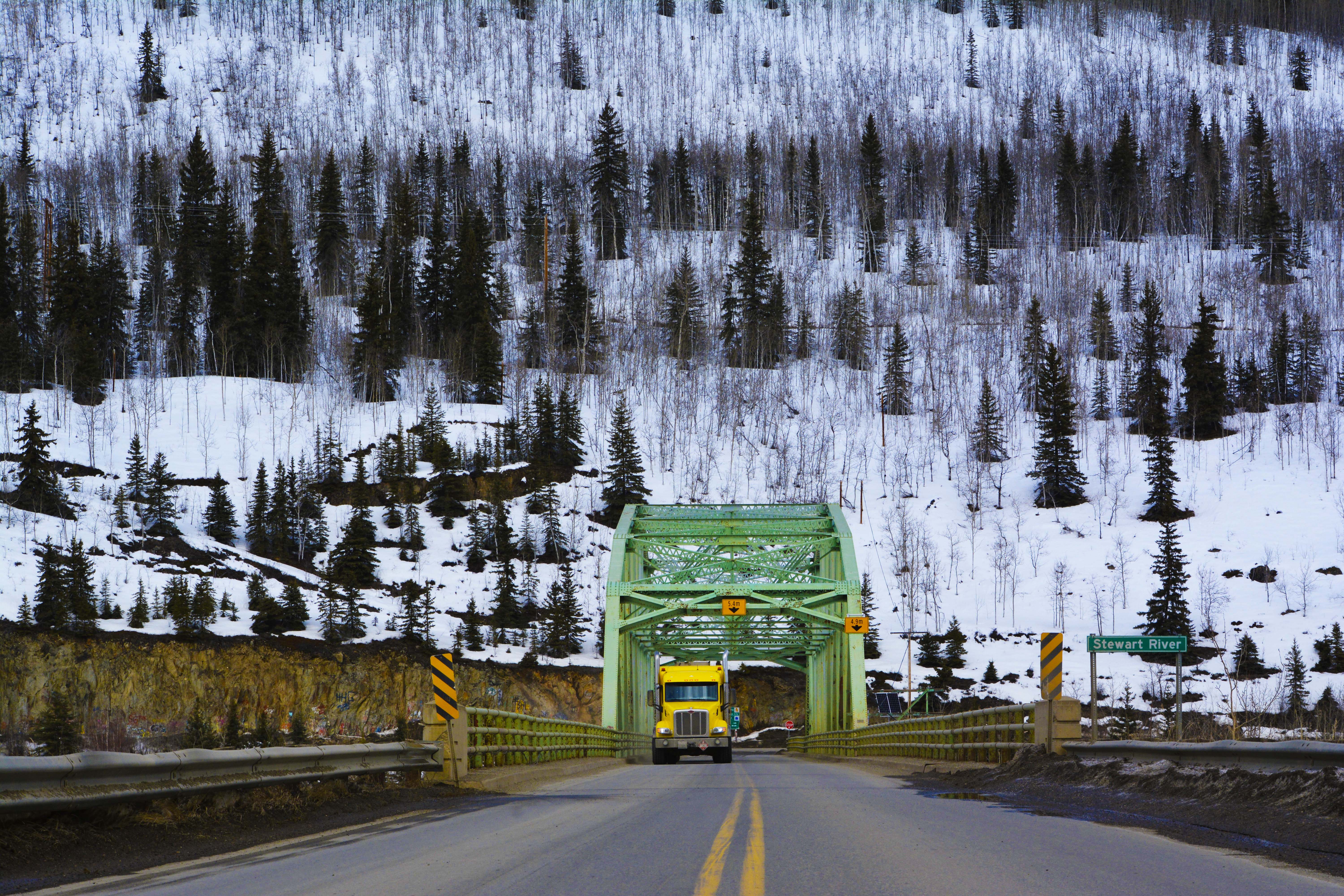 Yellow AFD Petroleum tanker truck crossing a green steel truss bridge over the Stewart River
