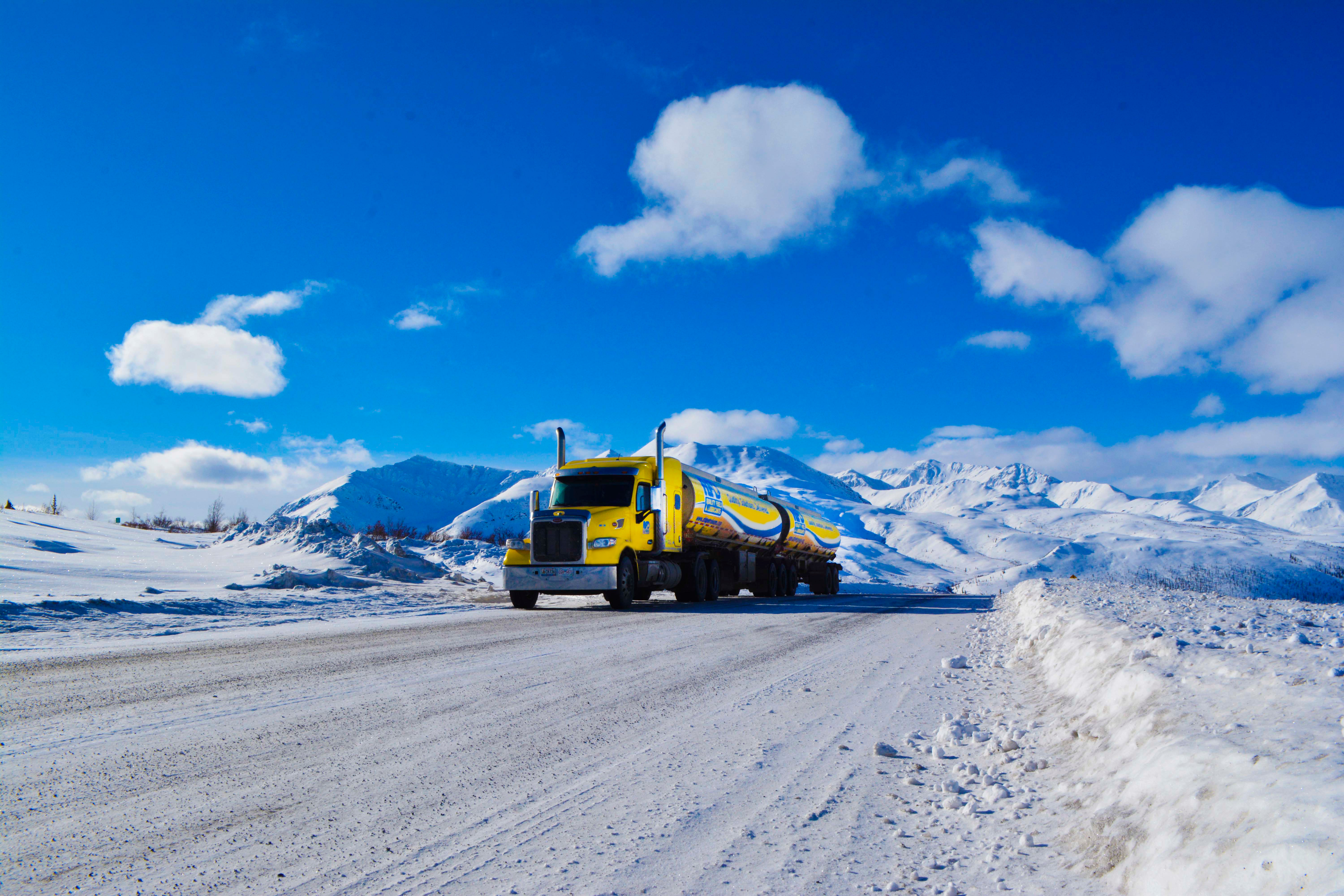 Yellow AFD Petroleum tanker truck driving through a snowy mountainous Yukon landscape under a blue sky