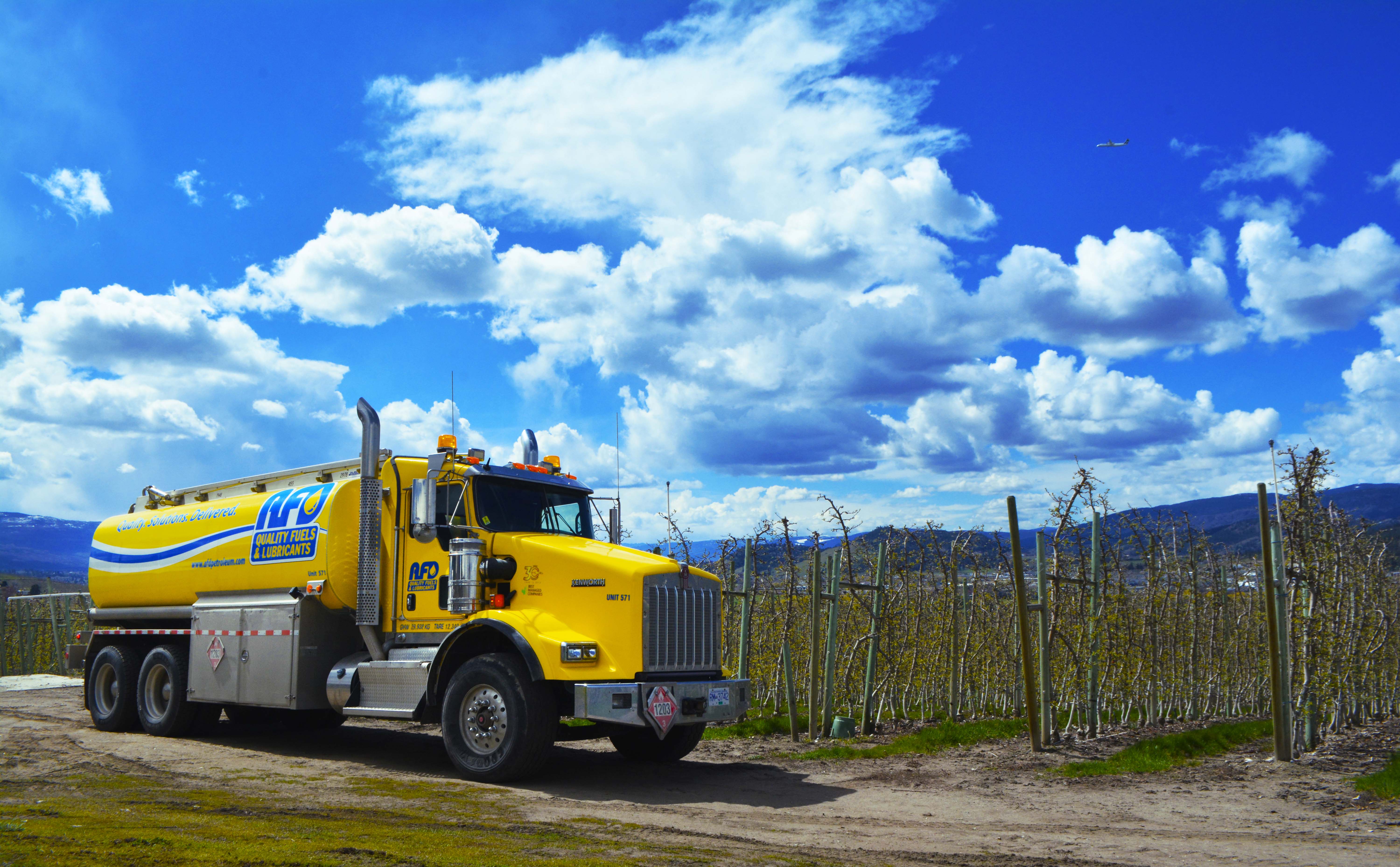 AFD Petroleum fuel tanker truck parked along a dirt road beside a young orchard