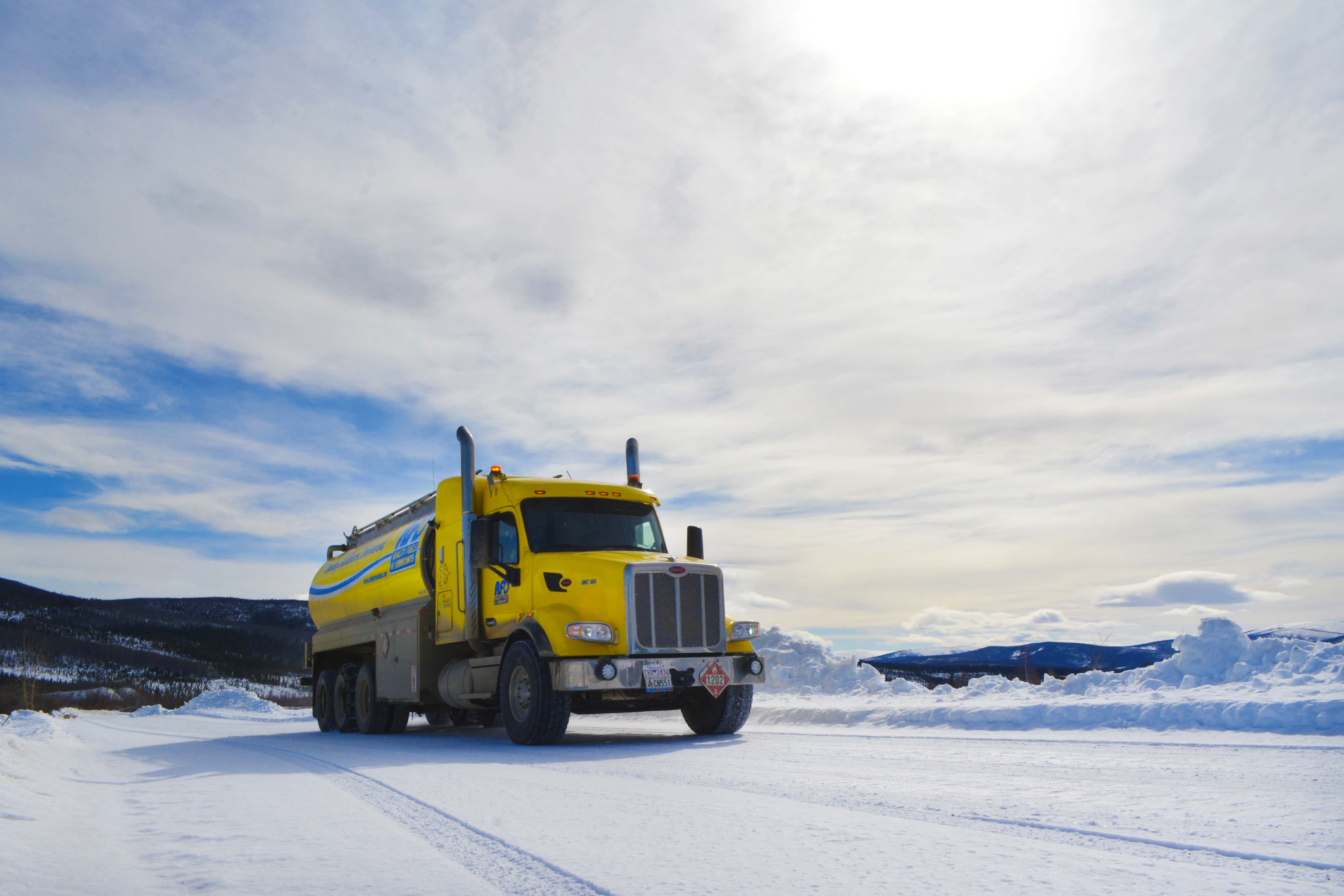 Yellow AFD Petroleum tanker truck driving on a snowy road under a bright blue Yukon sky